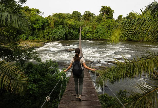 Traveller crossing rainforest suspension bridge in Cameroon 