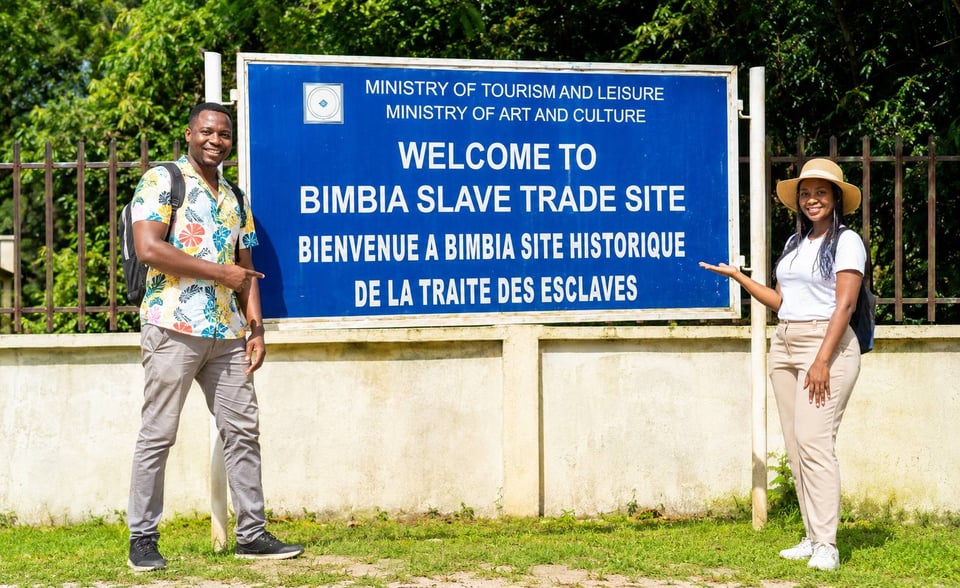 Two Tourists Pointing Towards The Bimbia Slave Trade Site Board
